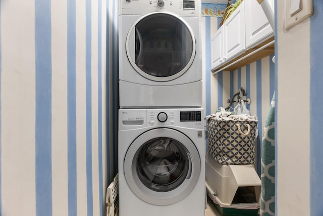 laundry area with wallpapered walls, stacked washer / dryer, and cabinet space