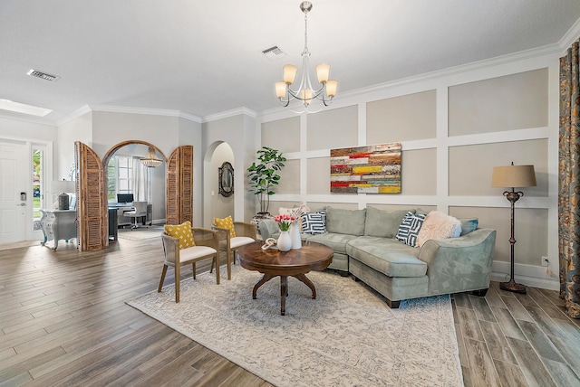 living area with a decorative wall, wood finished floors, visible vents, and ornamental molding