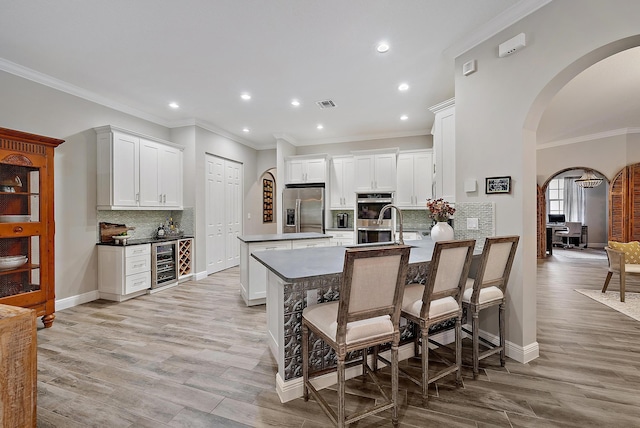 kitchen featuring visible vents, a peninsula, arched walkways, stainless steel appliances, and wine cooler