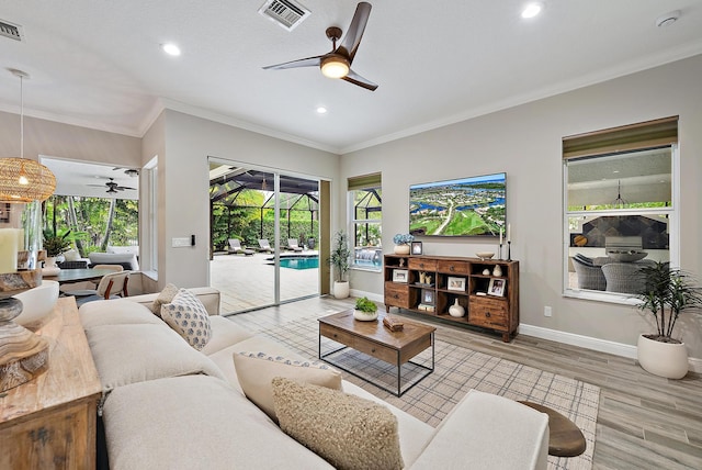 living area with visible vents, ornamental molding, a ceiling fan, a sunroom, and light wood finished floors