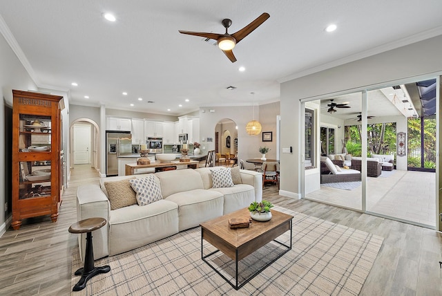 living area featuring crown molding, recessed lighting, light wood-style floors, and arched walkways