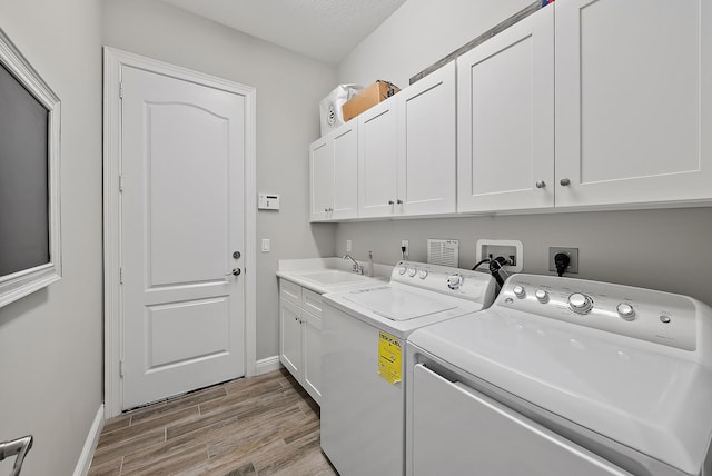 clothes washing area with baseboards, light wood-type flooring, separate washer and dryer, cabinet space, and a sink