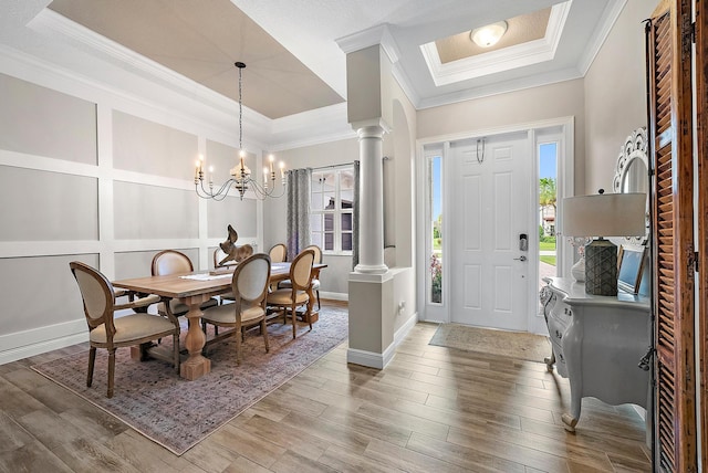 entrance foyer with a decorative wall, light wood-style floors, a tray ceiling, and decorative columns