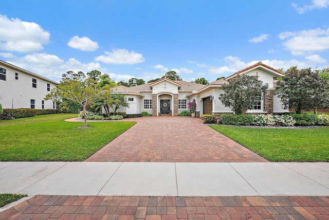 mediterranean / spanish-style house with a tile roof, a front yard, stucco siding, decorative driveway, and stone siding