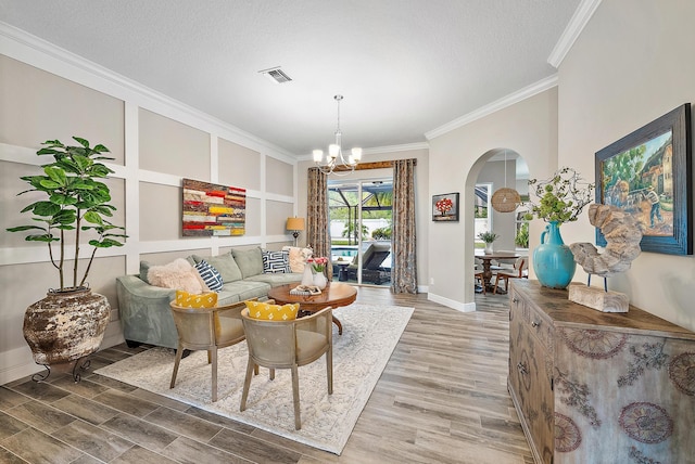 living area with wood finished floors, visible vents, arched walkways, ornamental molding, and a chandelier