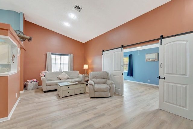 living room featuring baseboards, visible vents, high vaulted ceiling, light wood-style flooring, and a barn door