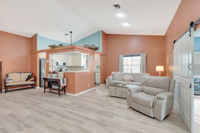 living area featuring visible vents, baseboards, light wood-type flooring, lofted ceiling, and a barn door