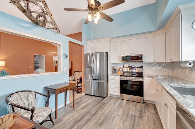 kitchen featuring light wood finished floors, appliances with stainless steel finishes, white cabinetry, and light stone countertops