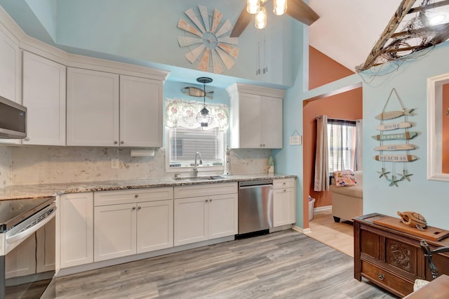 kitchen with light wood finished floors, light stone counters, appliances with stainless steel finishes, white cabinetry, and a sink