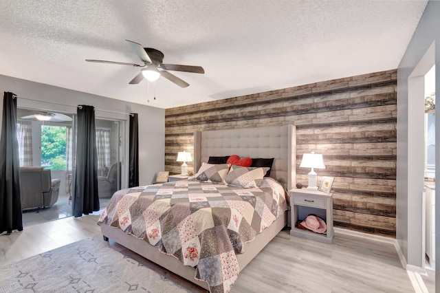 bedroom featuring wooden walls, light wood-style flooring, a textured ceiling, a ceiling fan, and access to outside