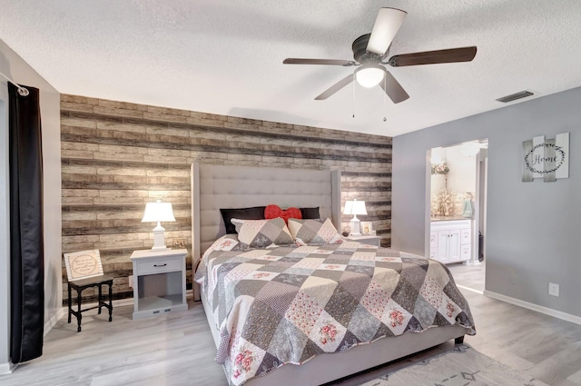 bedroom with visible vents, light wood-style floors, wood walls, a textured ceiling, and an accent wall