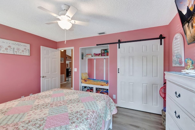 bedroom featuring visible vents, ceiling fan, a barn door, light wood-style floors, and a textured ceiling