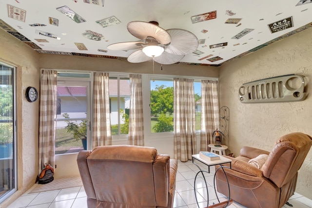 sitting room featuring light tile patterned floors, a ceiling fan, and a textured wall