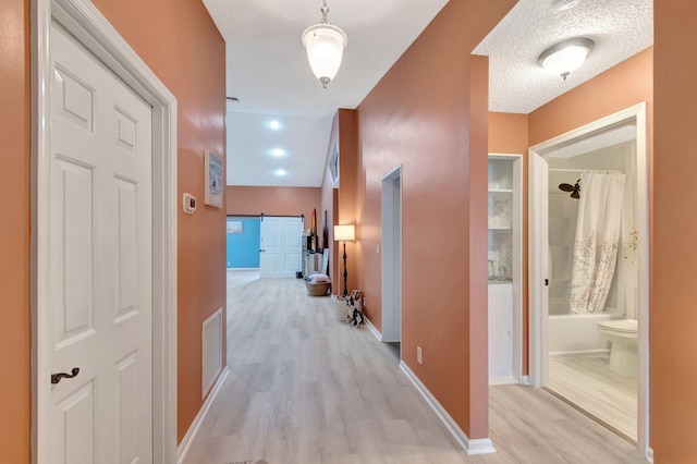 hallway with light wood finished floors, visible vents, a barn door, and baseboards