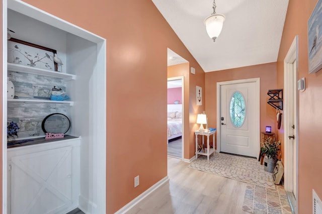 foyer with visible vents, baseboards, light wood-style floors, and vaulted ceiling