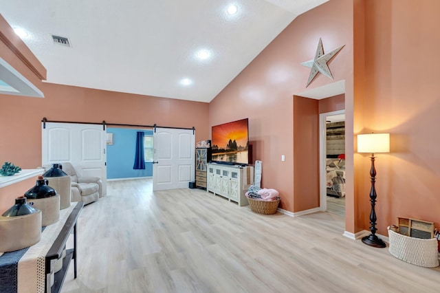 living area with wood finished floors, visible vents, baseboards, high vaulted ceiling, and a barn door