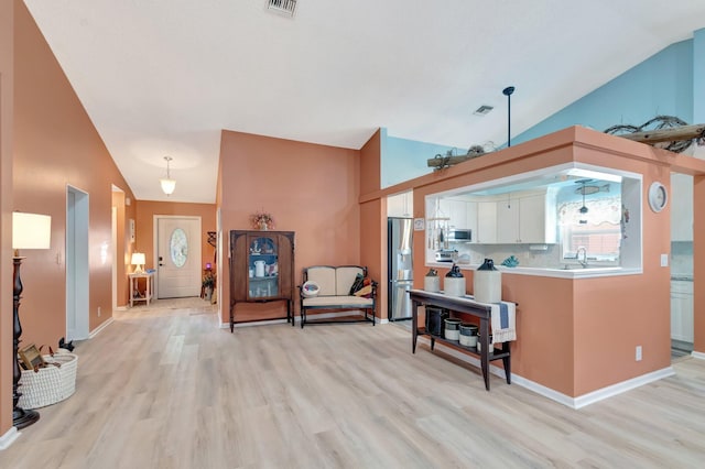 kitchen with vaulted ceiling, white cabinets, light wood-type flooring, and appliances with stainless steel finishes