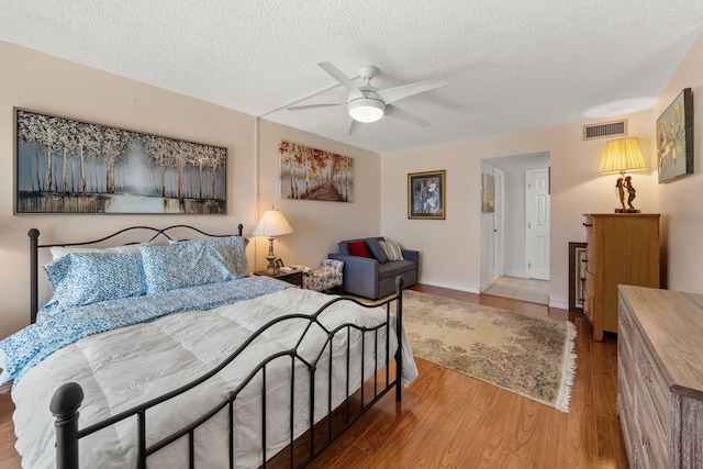 bedroom with visible vents, a ceiling fan, a textured ceiling, wood finished floors, and baseboards