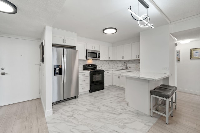 kitchen featuring a sink, stainless steel appliances, a peninsula, white cabinets, and decorative backsplash