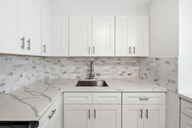 kitchen with light stone counters, white cabinets, backsplash, and a sink
