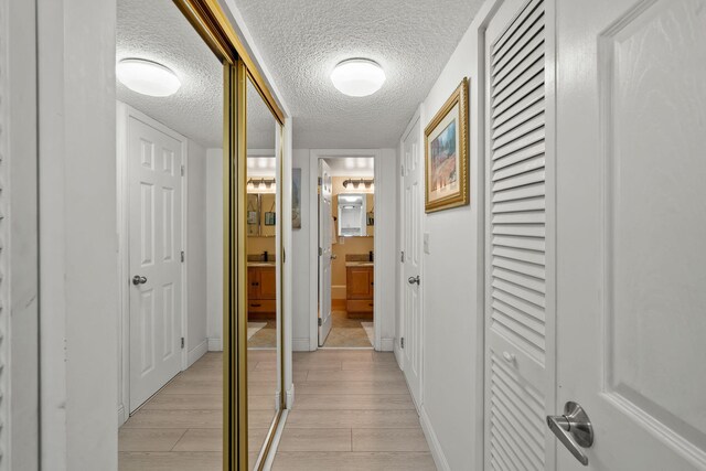 corridor with light wood-style floors, baseboards, and a textured ceiling