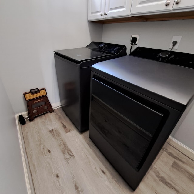 clothes washing area with baseboards, cabinet space, light wood-style floors, and washing machine and clothes dryer