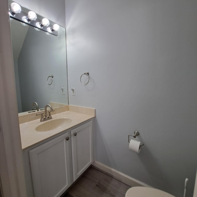 bathroom with toilet, vanity, baseboards, and wood finished floors