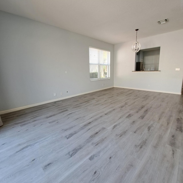 unfurnished living room featuring visible vents, an inviting chandelier, baseboards, and wood finished floors