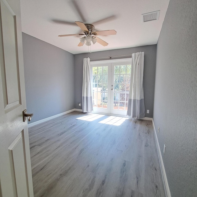 empty room featuring visible vents, baseboards, wood finished floors, french doors, and a textured wall