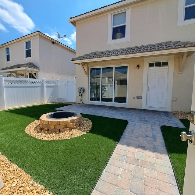 rear view of property featuring a patio, fence, a yard, stucco siding, and a fire pit