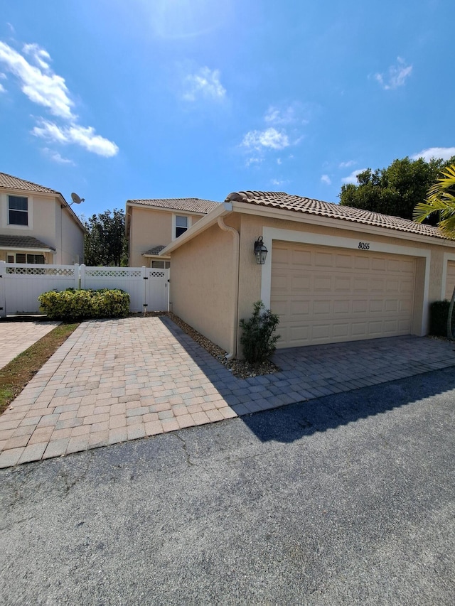 view of front of property featuring stucco siding, a gate, fence, a garage, and a tiled roof