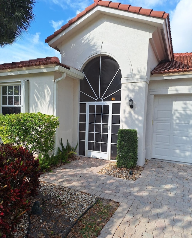 entrance to property featuring stucco siding, a tile roof, and a garage