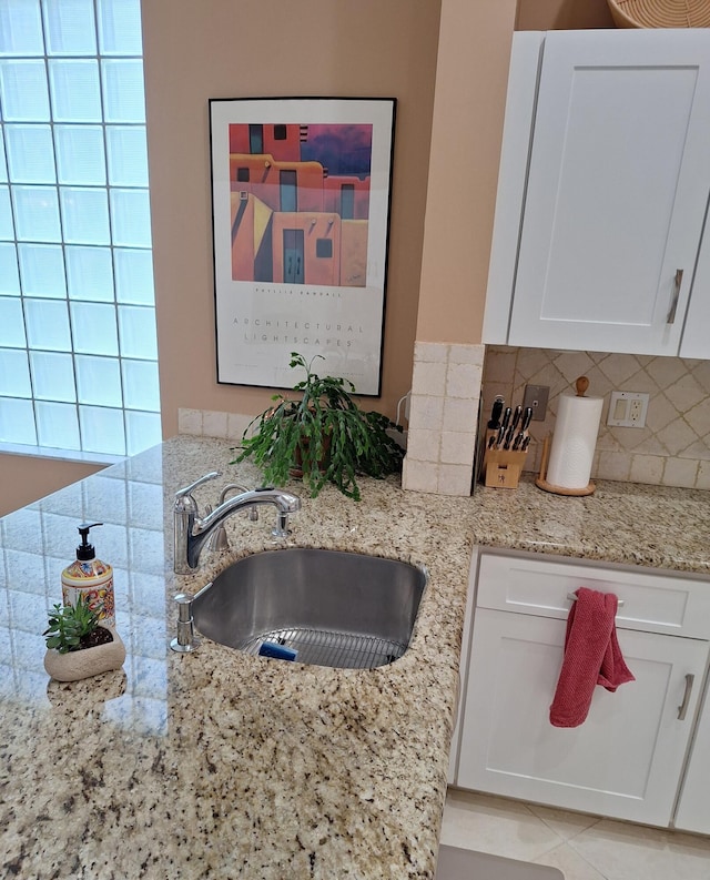 kitchen with a sink, white cabinetry, light tile patterned floors, decorative backsplash, and light stone countertops