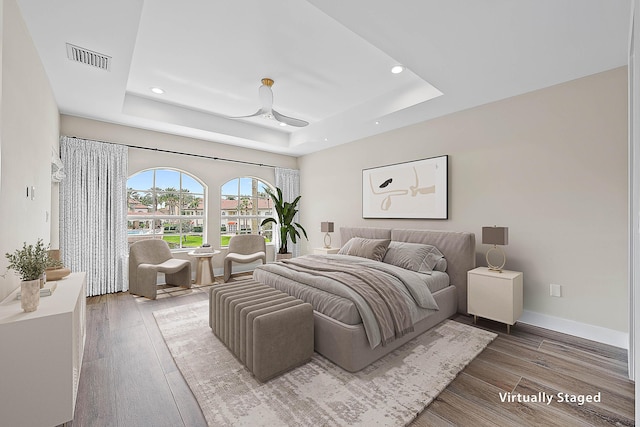 bedroom with visible vents, baseboards, a tray ceiling, recessed lighting, and wood finished floors