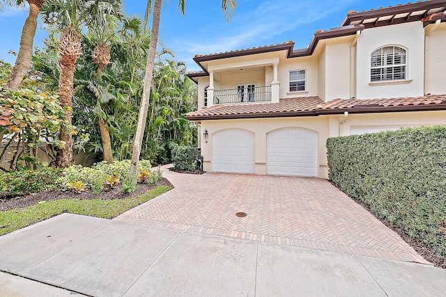 mediterranean / spanish home featuring stucco siding, decorative driveway, a garage, a balcony, and a tiled roof