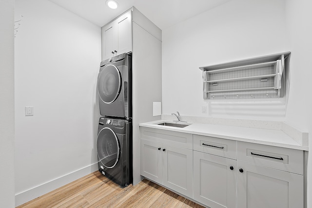 clothes washing area featuring baseboards, cabinet space, a sink, light wood-style floors, and stacked washer / dryer