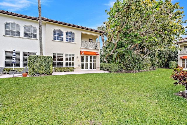 rear view of property featuring a balcony, stucco siding, french doors, a patio area, and a lawn