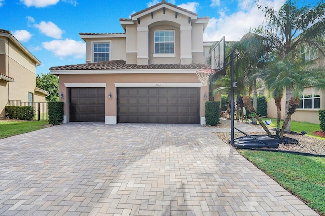 mediterranean / spanish-style house with fence, a tile roof, stucco siding, decorative driveway, and a garage