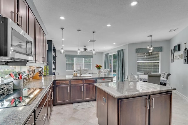 kitchen featuring a sink, stainless steel microwave, light stone counters, a peninsula, and black electric cooktop