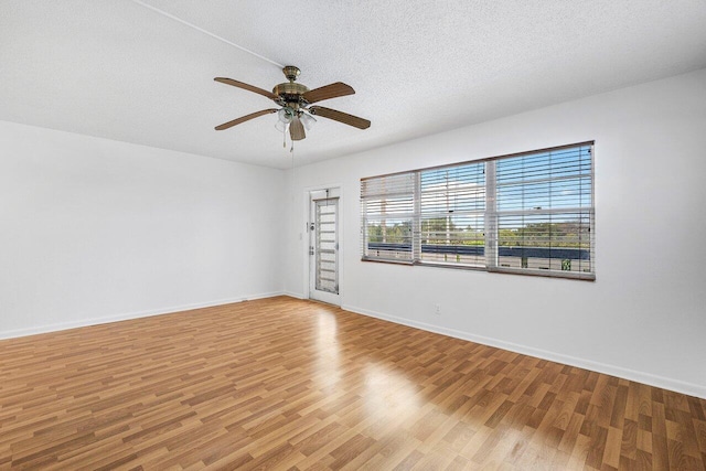 spare room with a textured ceiling, light wood-type flooring, a ceiling fan, and baseboards