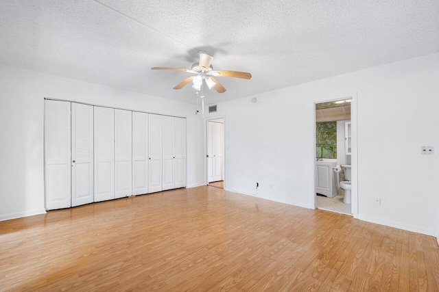 unfurnished bedroom featuring light wood finished floors, visible vents, a ceiling fan, ensuite bath, and a textured ceiling