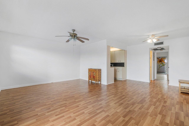 unfurnished living room with light wood finished floors, visible vents, a ceiling fan, and a textured ceiling