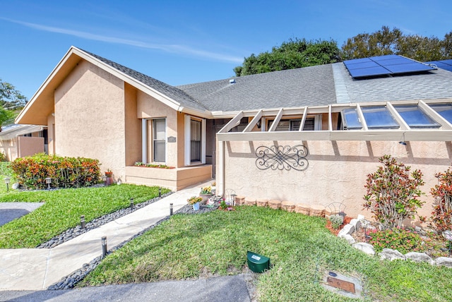 exterior space featuring solar panels, a front yard, roof with shingles, and stucco siding