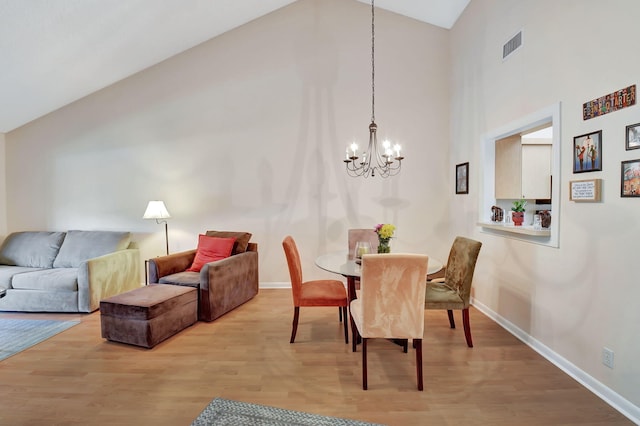 dining room featuring visible vents, baseboards, wood finished floors, a notable chandelier, and high vaulted ceiling