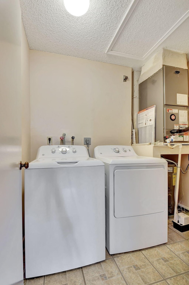 clothes washing area with heating unit, a textured ceiling, laundry area, and washer and clothes dryer