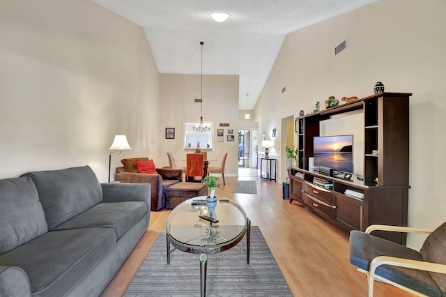 living room with a notable chandelier, light wood-style flooring, and high vaulted ceiling