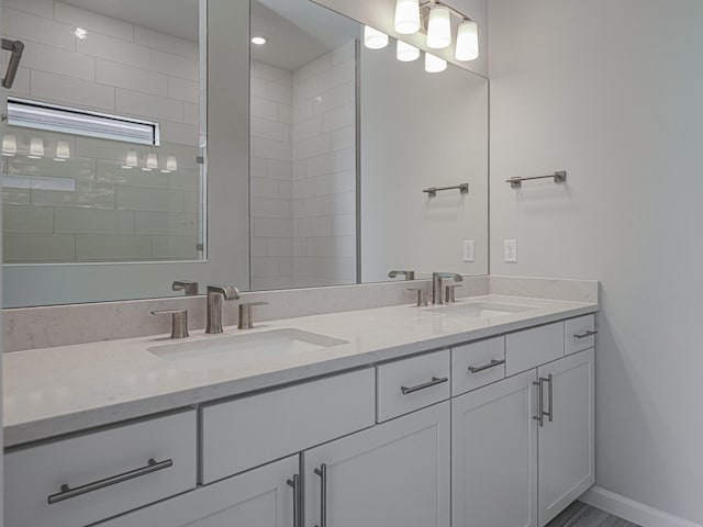 full bathroom with double vanity, a tile shower, baseboards, and a sink