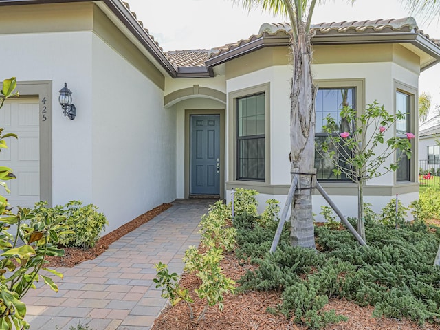 view of exterior entry with stucco siding, a tile roof, and a garage