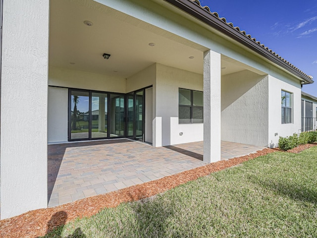 view of exterior entry with stucco siding, a tile roof, a lawn, and a patio