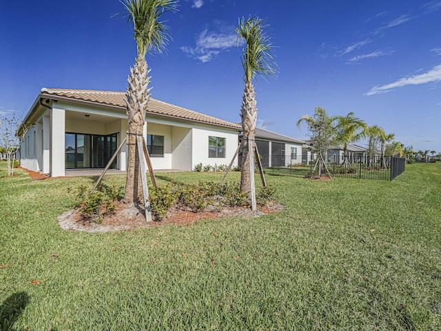 back of property featuring stucco siding, a lawn, a tile roof, and fence